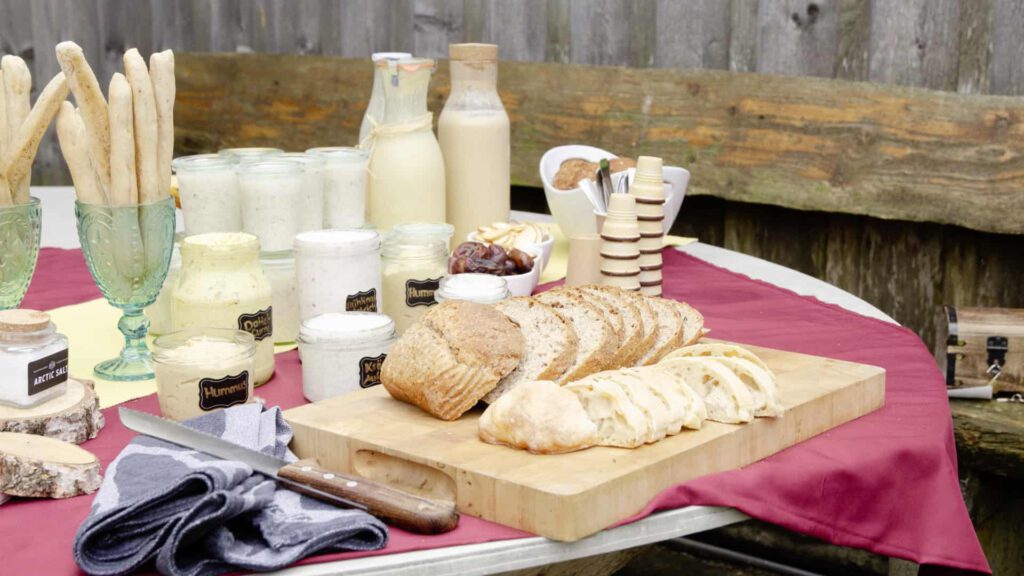 Frisches Brot, verschiedene Aufstriche, Müsli und Smoothies stehen drapiert auf einem Tisch.